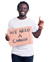 Young african american man with braids holding we need a change banner surprised with an idea or question pointing finger with happy face, number one