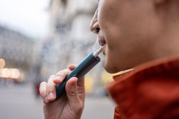 Close up of a man vaping with electronic cigarette outdoor on street. 