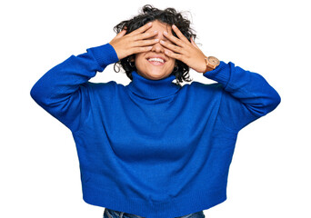 Young hispanic woman with curly hair wearing turtleneck sweater covering eyes with hands smiling cheerful and funny. blind concept.