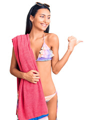 Young beautiful latin girl wearing bikini and sunglasses pointing thumb up to the side smiling happy with open mouth