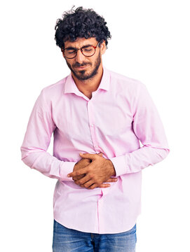 Handsome young man with curly hair and bear wearing business clothes with hand on stomach because nausea, painful disease feeling unwell. ache concept.