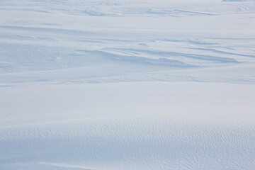 Beautiful winter background with snowy ground. Natural snow texture. Wind sculpted patterns on snow surface.
