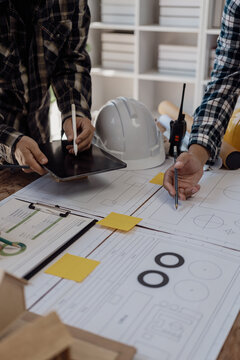 Construction site engineers are reviewing blueprints on sheets of paper and planning to work together to build a building on site. vertical picture