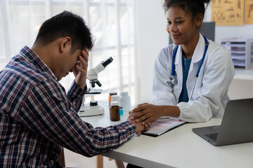 Young Asian man discusses illness with African female doctor in hospital, medical health concept