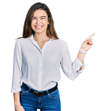 Young caucasian girl wearing casual white shirt with a big smile on face, pointing with hand finger to the side looking at the camera.