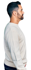 Young hispanic man with beard wearing casual white sweater looking to side, relax profile pose with natural face with confident smile.