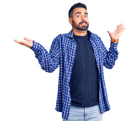 Young hispanic man wearing casual clothes clueless and confused expression with arms and hands...