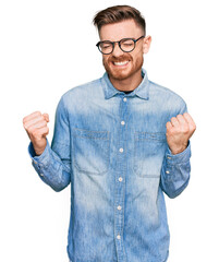 Young redhead man wearing casual denim shirt excited for success with arms raised and eyes closed celebrating victory smiling. winner concept.