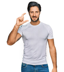 Fototapeta premium Young hispanic man wearing casual white t shirt smiling and confident gesturing with hand doing small size sign with fingers looking and the camera. measure concept.
