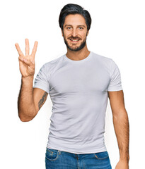 Young hispanic man wearing casual white t shirt showing and pointing up with fingers number three while smiling confident and happy.