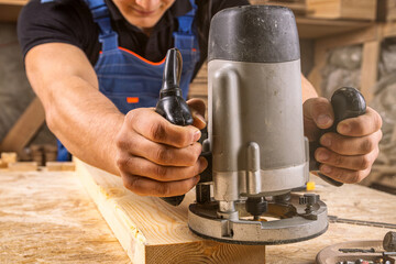 A strong male carpenter  in work clothes enthusiastically works and saws a wooden board on a wooden...