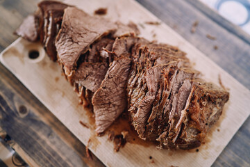 Thin slices of juicy roast beef lie in a row on a wooden cutting board