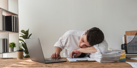Obraz premium Unhappy young office worker feeling bored at work looking at laptop with a hopeless expression while sitting in the office. Male office worker feeling tired from monotonous work.