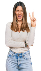 Young woman wearing casual clothes smiling with happy face winking at the camera doing victory sign. number two.