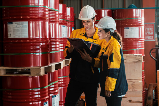 Two factory workers or inventory inspector conduct professional inspection on hazardous chemical barrels in warehouse, chemistry storage workplace and industrial profession concept. Exemplifying