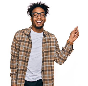 Young african american man with beard wearing casual clothes and glasses with a big smile on face, pointing with hand finger to the side looking at the camera.