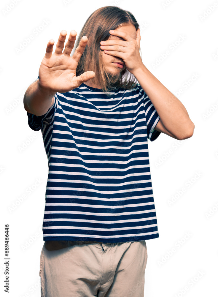 Wall mural Handsome caucasian man with long hair wearing casual striped t-shirt covering eyes with hands and doing stop gesture with sad and fear expression. embarrassed and negative concept.