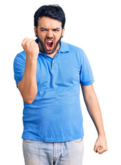 Fototapeta premium Young hispanic man wearing casual clothes angry and mad raising fist frustrated and furious while shouting with anger. rage and aggressive concept.