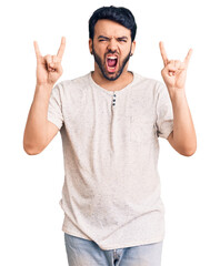 Fototapeta premium Young hispanic man wearing casual clothes shouting with crazy expression doing rock symbol with hands up. music star. heavy concept.