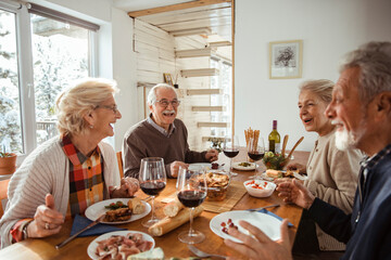 Group of senior people friends eating meal at cozy home during winter