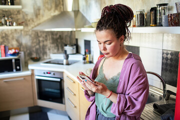 Young woman browsing on smartphone at home kitchen