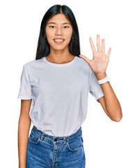 Beautiful young asian woman wearing casual white t shirt showing and pointing up with fingers number five while smiling confident and happy.
