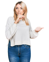 Young caucasian woman wearing casual winter sweater asking to be quiet with finger on lips pointing with hand to the side. silence and secret concept.