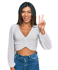 Young latin transsexual transgender woman wearing casual clothes smiling with happy face winking at the camera doing victory sign with fingers. number two. - obrazy, fototapety, plakaty