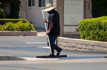 A man in a straw hat spreading new asphalt slurry