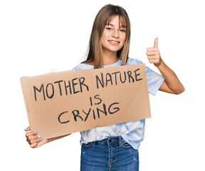 Teenager caucasian girl holding mother nature is crying protest cardboard banner smiling happy and positive, thumb up doing excellent and approval sign