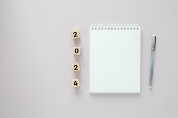 Flat lay of an open blank white page of a notepad with a pen on a side and numbers 2024 on wooden...