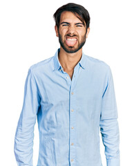 Hispanic man with blue eyes wearing business shirt sticking tongue out happy with funny expression. emotion concept.