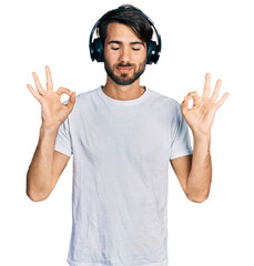 Hispanic man with blue eyes listening to music using headphones relax and smiling with eyes closed doing meditation gesture with fingers. yoga concept.