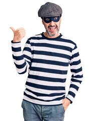 Middle age handsome man wearing burglar mask smiling with happy face looking and pointing to the...