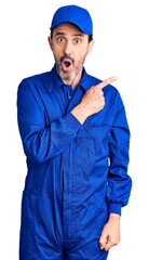 Middle age handsome man wearing mechanic uniform surprised pointing with finger to the side, open...