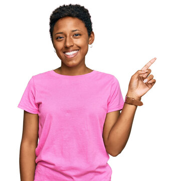 Young african american woman wearing casual clothes with a big smile on face, pointing with hand finger to the side looking at the camera.