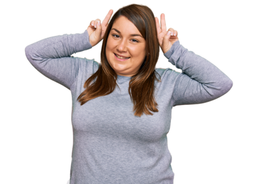 Beautiful brunette plus size woman wearing casual clothes posing funny and crazy with fingers on head as bunny ears, smiling cheerful