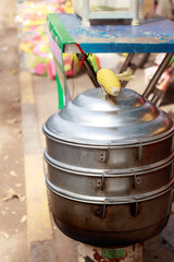 Fototapeta premium Vertical view of a metal steamer for cooking whole corn cob at the sidewalk, a popular khmer streetfood in Kampot, Cambodia