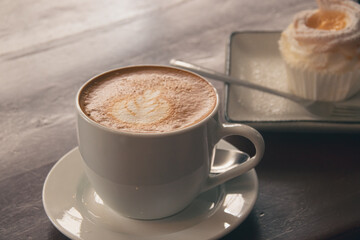 A cup of coffee with latte art beside a brazo de mercedez cupcake, a popular authentic Filipino pastry in the Philippines