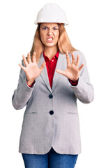 Beautiful young woman wearing architect hardhat disgusted expression, displeased and fearful doing disgust face because aversion reaction. with hands raised