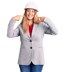 Beautiful young woman wearing architect hardhat smiling cheerful showing and pointing with fingers teeth and mouth. dental health concept.