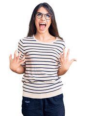 Brunette teenager girl wearing casual clothes and glasses crazy and mad shouting and yelling with aggressive expression and arms raised. frustration concept.