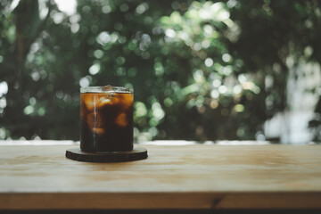 Cold black coffee with ice cubes on a wood table against nature background. Cold Brew. Summer...