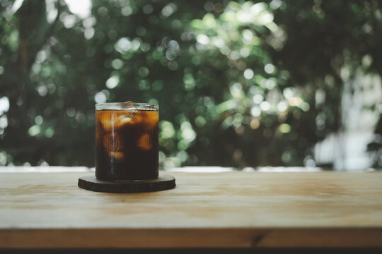 Cold Black Coffee With Ice Cubes On A Wood Table Against Nature Background. Cold Brew. Summer Drinks.