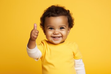 Portrait of a cute african american baby boy showing thumbs up over yellow background, a toddler giving a thumbs up on yellow background, AI Generated - Powered by Adobe