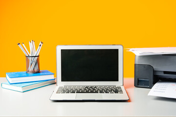 Laser printer and laptop on desk against yellow background