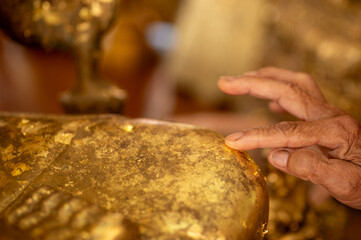 hand gliding gold leaf on buddha statue, Thai tradition cover statue of Buddha with gold leaf