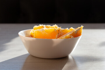 Picture of juicy fresh orange wedges in a bowl. Healthy snack on the kitchen table. Beautiful bright sunlight. Summer fruit