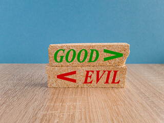 Concept green word Good and Evil on brick blocks. Beautiful wooden table, blue background. Sign...