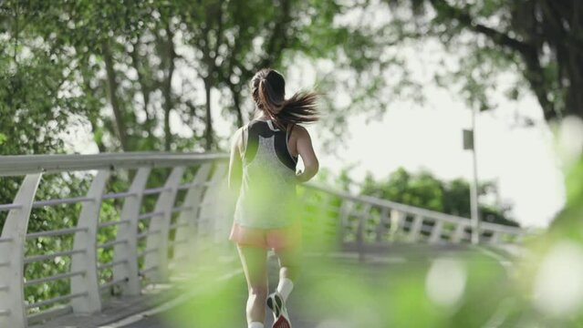 rear view of a young asian woman running jogging outdoors on road in park